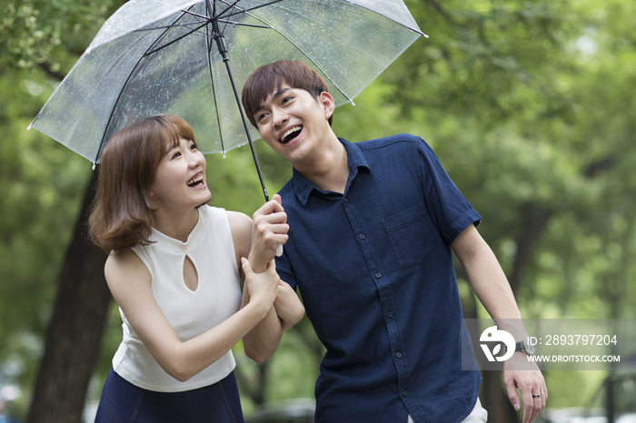 快乐的年轻情侣打着雨伞散步