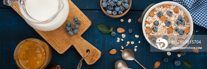 A healthy breakfast on a dark blue wooden background: Oatmeal, milk, blueberries, honey and almonds.