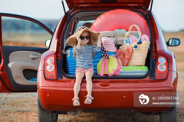 Little girl in straw hat sitting in the trunk of a car