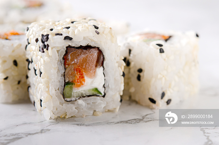 Sushi roll sushi with salmon, cucumber, cream cheese, sesame seeds on a white marble table.