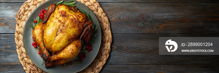 Baked chicken for festive dinner. Cooked chicken or turkey with herb rosemary and berries on wooden table. Thanksgiving holiday concept. Copy space