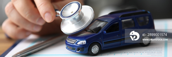 Close-up of male hand holding stethoscope and examining passenger car. Vehicle on important documents of insurance. Advertisement of service station concept