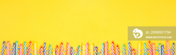 Birthday cake candles with candy sprinkles. Top down view banner with bottom border on a yellow background. Copy space.