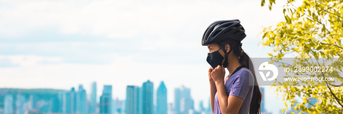 Wearing covid-19 mask while riding bike. Sport cyclist woman biking putting on face mask for Covid-19 prevention during summer outdoor leisure exercise activity. Fitness outside.