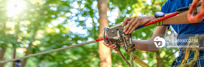 Woman hangs a carabiner on a rope in a forest adventure park. Using climbing equipment: carabiner, belt, rope. Banner for advertising, design or website header