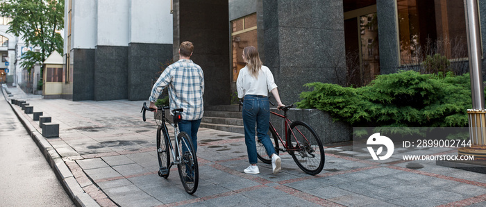 Back view of man and girl walking with bicycles