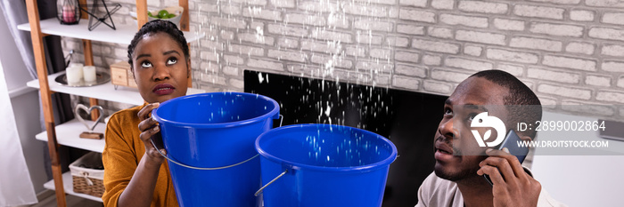 Couple Using Bucket For Collecting Water Leakage From Ceiling