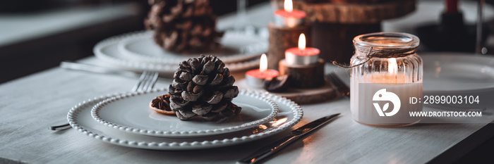 Rustic table decor for Christmas or New Year family dinner. Centrepiece with red candle, dry orange, cone, cinnamon, anise. Zero waste eco-friendly home. Cozy atmosphere, dark background. Banner