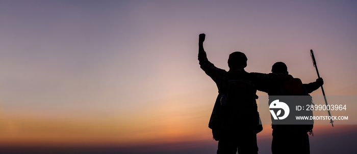 Silhouette of cheering hiking couple open arms to the sunrise stand at on mountain