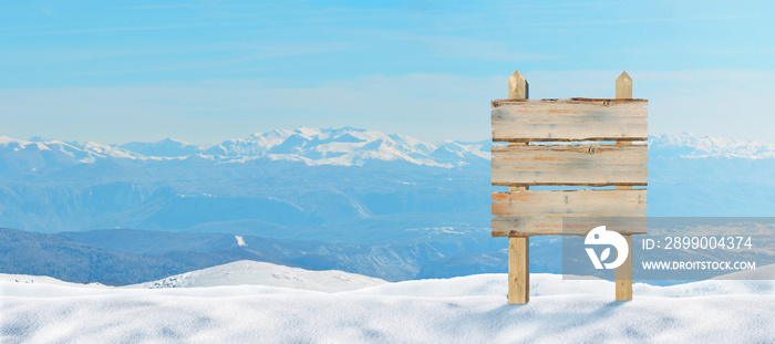 Wooden signpost at the top of the mountain pinned into the snow. Snowy peaks in the background