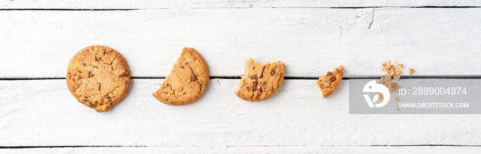 Five steps of chocolate chip cookies being devoured on white wooden table. Top view. Banner