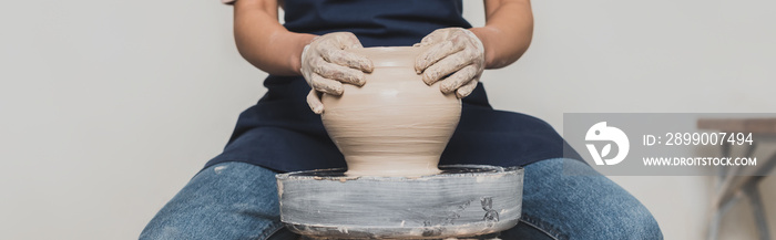 partial view of young african american woman in apron sitting on bench and shaping wet clay pot in pottery, banner