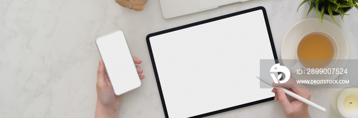 Overhead of female freelancer working on blank screen tablet and smartphone on marble table