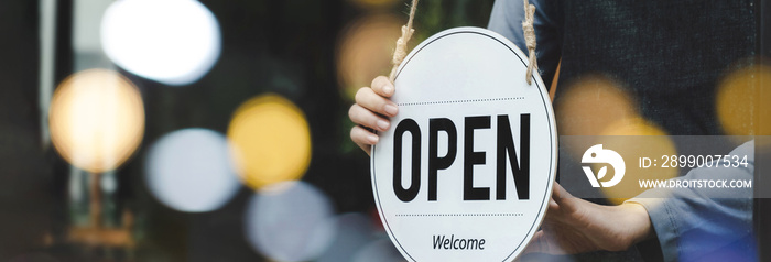 Welcome. waitress staff woman turning wooden open sign board on glass door with bokeh ligh in modern cafe coffee shop, cafe restaurant, retail store, small business owner, food and drink concept