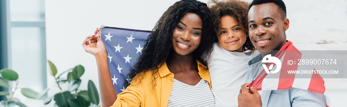 horizontal crop of african american family covered with flag of america looking at camera