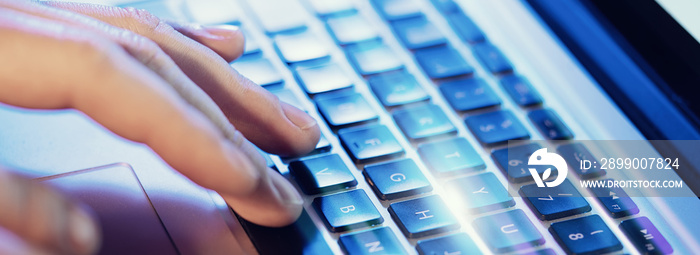 Closeup of male hands typing on laptop keyboard at the office. Visual effects, flares. Wide