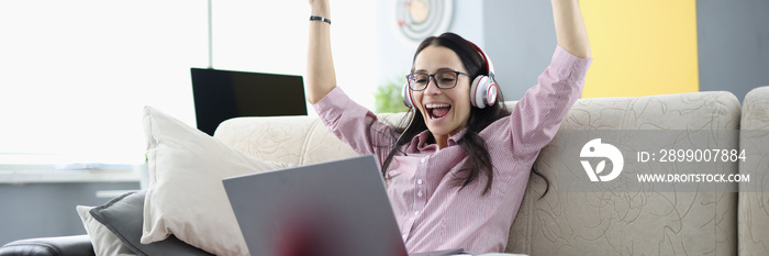 Rejoicing woman is sitting on sofa with in headphones with laptop. Positive and joyful time at home concept