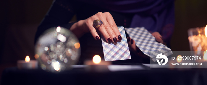 Close-up of fortuneteller’s hands with cards at table with candles, magic ball in dark room