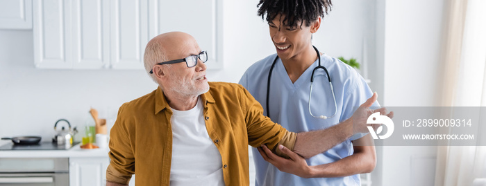 Positive pensioner talking to african american nurse at home, banner.