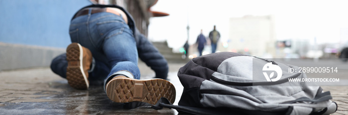 Man with backpack lying on slippery sidewalk after fall closeup