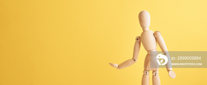 Wooden doll with gesture on yellow background. Mannequin shows gesture. Figure of wooden human with copy space