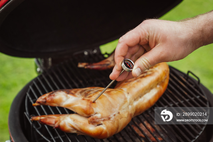 Men chef measuring rabbit meat temperature. Gourmet barbecue- smoking, baking, roasting process. Cer