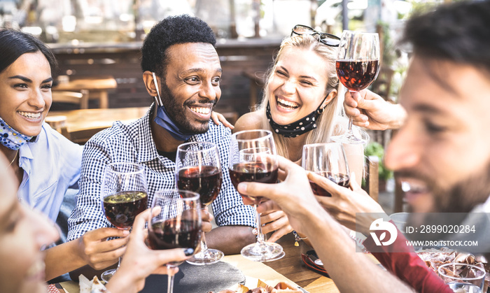 Friends toasting red wine at outdoor restaurant bar with open face mask - New normal lifestyle conce
