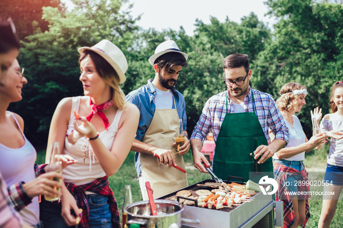 Young friends having fun grilling meat enjoying barbecue party.