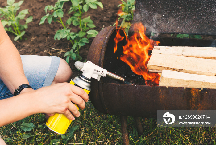 Close up man holds a gas burner with a balloon and makes a fire in the grill. Flame gun on the backg