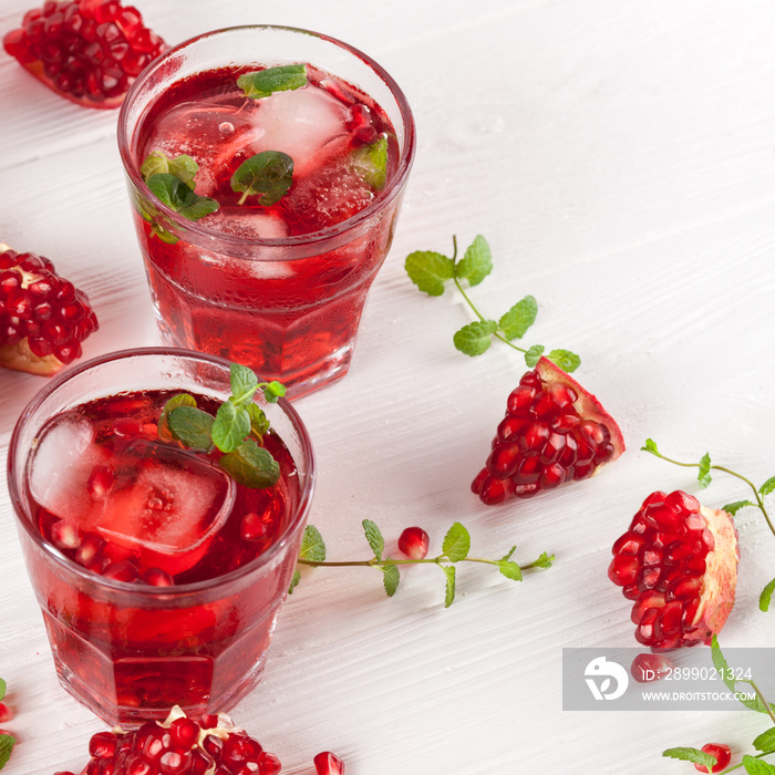 Pomegranate cocktail with ice and mint in beautiful glasses and jug, fresh ripe pomegranate on white