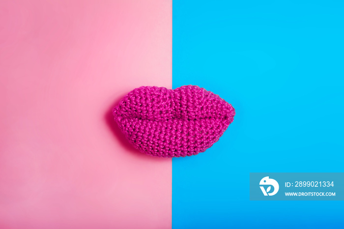 A kiss as a symbol of the combination of men and women. Knitted lips on a blue and pink background.