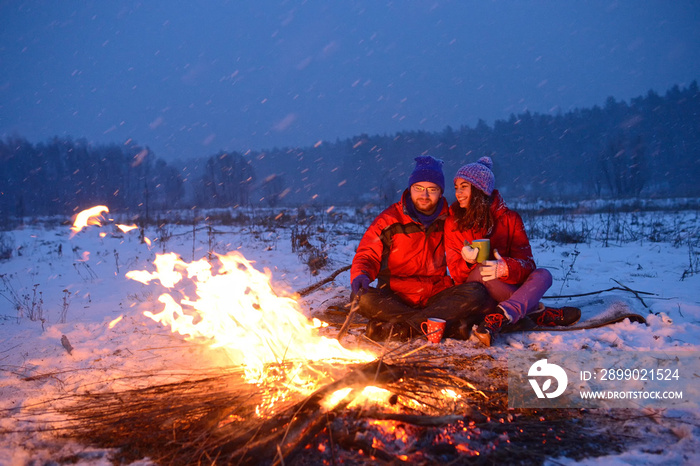 Happy loving couple sitting at a fire in the snow among the fields in the winter            against 