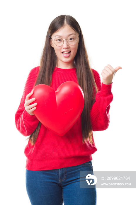 Young Chinese woman wearing graduate uniform red heart pointing and showing with thumb up to the sid