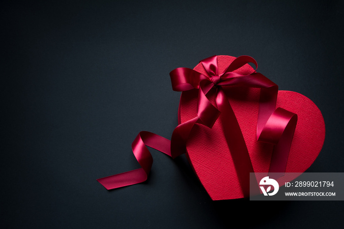 Red gift box heart shape with red ribbon on a black background, gift concept