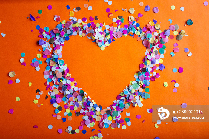 love concept image of heart shape frame made of colorful confetti on orange paper texture background