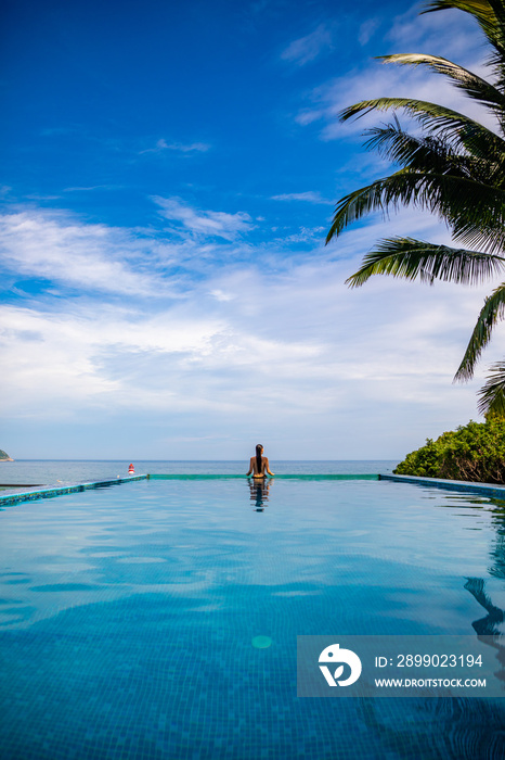 Woman relaxing in infinity swimming pool with sea view, vacation in tropics