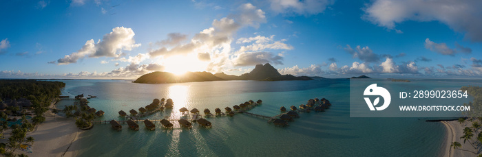 Panoramic aerial view of luxury overwater villas with palm trees, blue lagoon, white sandy beach and