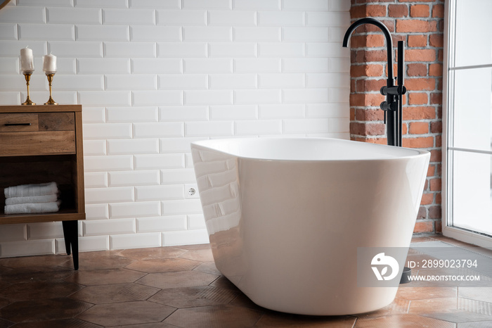 Modern bathroom with freestanding white acrylic bathtub and black loft mixer. Walls made of bricks, 