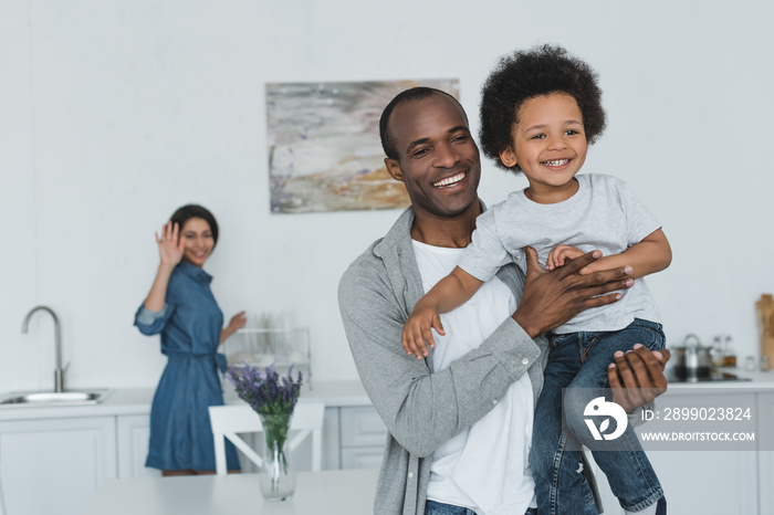 african american father hugging son and mother waving hand at home