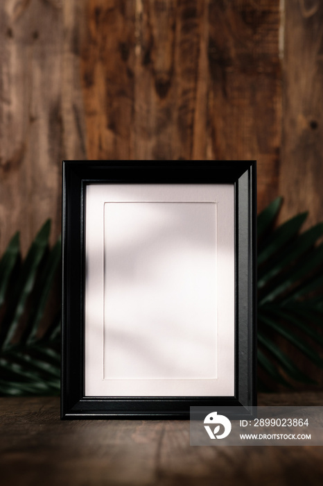 blank black photo frame on wood table and wall witn sunlight from window