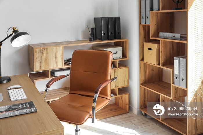 Interior of light office with desk, chair and shelving unit