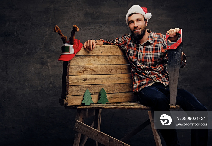 Positive male sits on wooden palette and  holds handsaw.