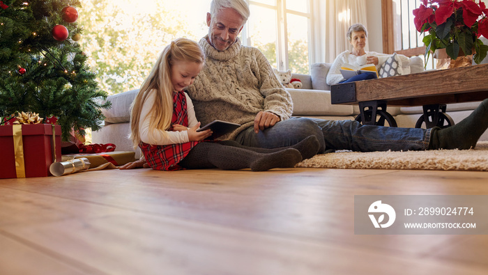 Senior man with granddaughter using digital tablet at home