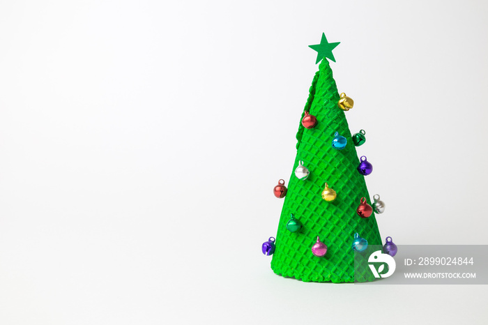 Green ice cream cone in form of Christmas tree decorated with colorful baubles and star on white bac