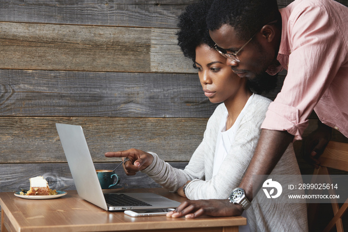 Two young colleagues using laptop. Double exposure of African boss dressed in formal wear, watching 