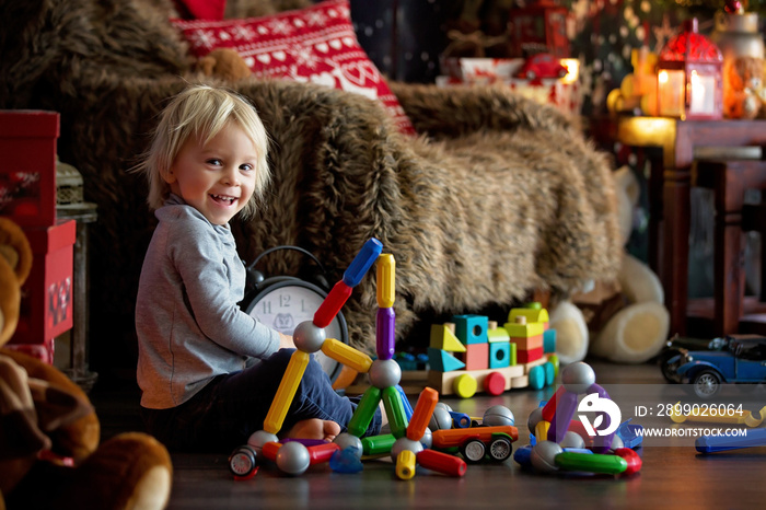 Sweet blonde toddler boy, playing with plastic construction, making different shapes