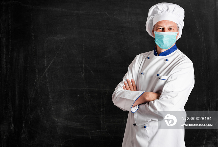 Masked chef in front of an empty blackboard, coronavirus restaurant concept