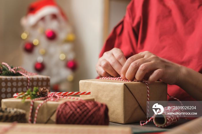 woman making Christmas handmade gift box with brown paper warpping with xmas decor on wood table