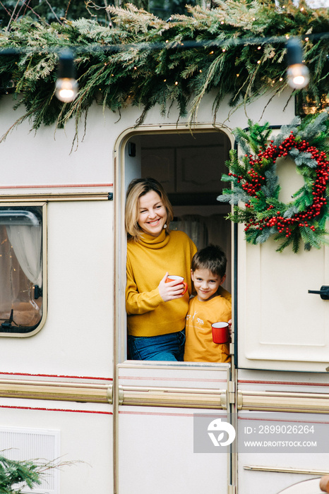 Beautiful mother and child boy with red cups drink cocoa or tea in trailer. Family vacation RV holid