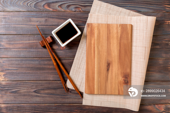 Empty rectangular wooden plate for sushi with sauce and chopsticks on wooden table, top view